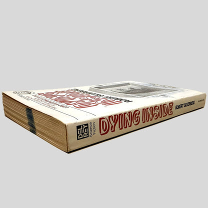 Close-up spine view of Dying Inside by Robert Silverberg centered on a neutral light gray background. Spine is square and shows minor chipping to spine edges, no creasing. Pages lay flat.