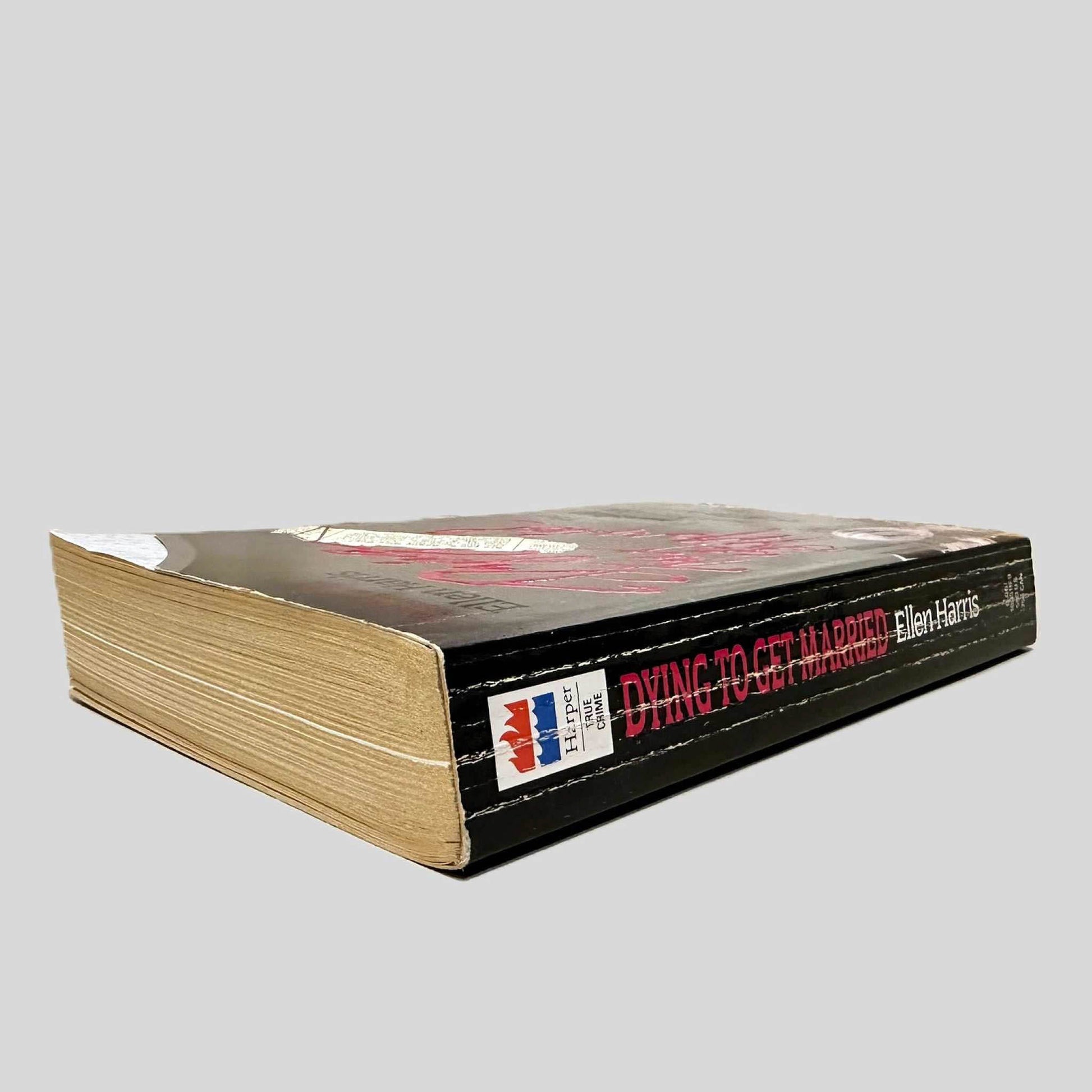 Close-up spine view of Dying to Get Married by Ellen Harris centered on a neutral light gray background. Spine is square and shows creasing. Pages lay flat.