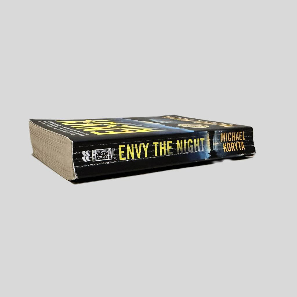 Close-up spine view of Envy the Night by Michael Koryta centered on a neutral light gray background. Spine shows creasing. Pages lay flat.