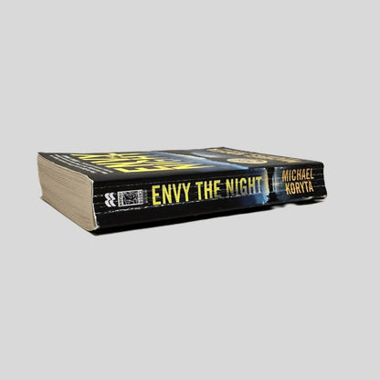Close-up spine view of Envy the Night by Michael Koryta centered on a neutral light gray background. Spine shows creasing. Pages lay flat.
