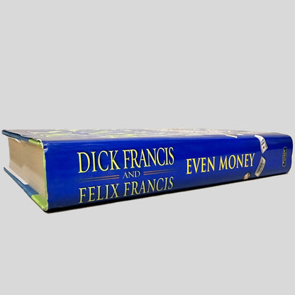 Close-up spine view of Even Money by Dick Francis & Felix Francis centered on a neutral light gray background. Dust jacket is present and shows no damage. Pages lay flat.
