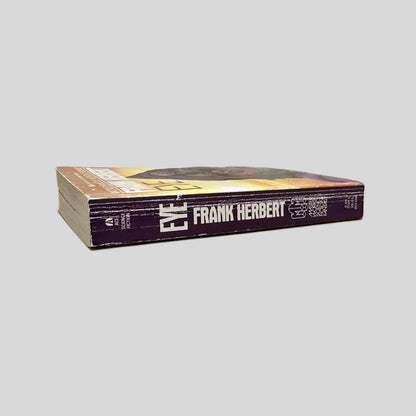 Close-up spine view of Eye by Frank Herbert centered on a neutral light gray background. Spine shows creasing and chipping to the top spine edge. Pages lay flat.