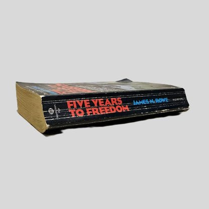 Close-up spine view of Five Years to Freedom: The True Story of a Vietnam POW by James N. Rowe centered on a neutral light gray background. Spine shows chipping and creasing. Pages lay flat.