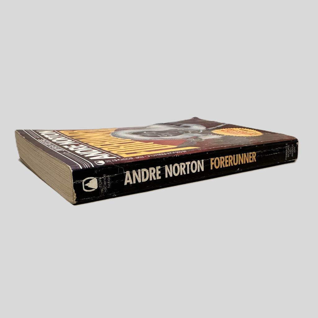 Close-up spine view of Forerunner by Andre Norton centered on a neutral light gray background. Spine shows normal chipping for age and creasing. Pages lay flat.