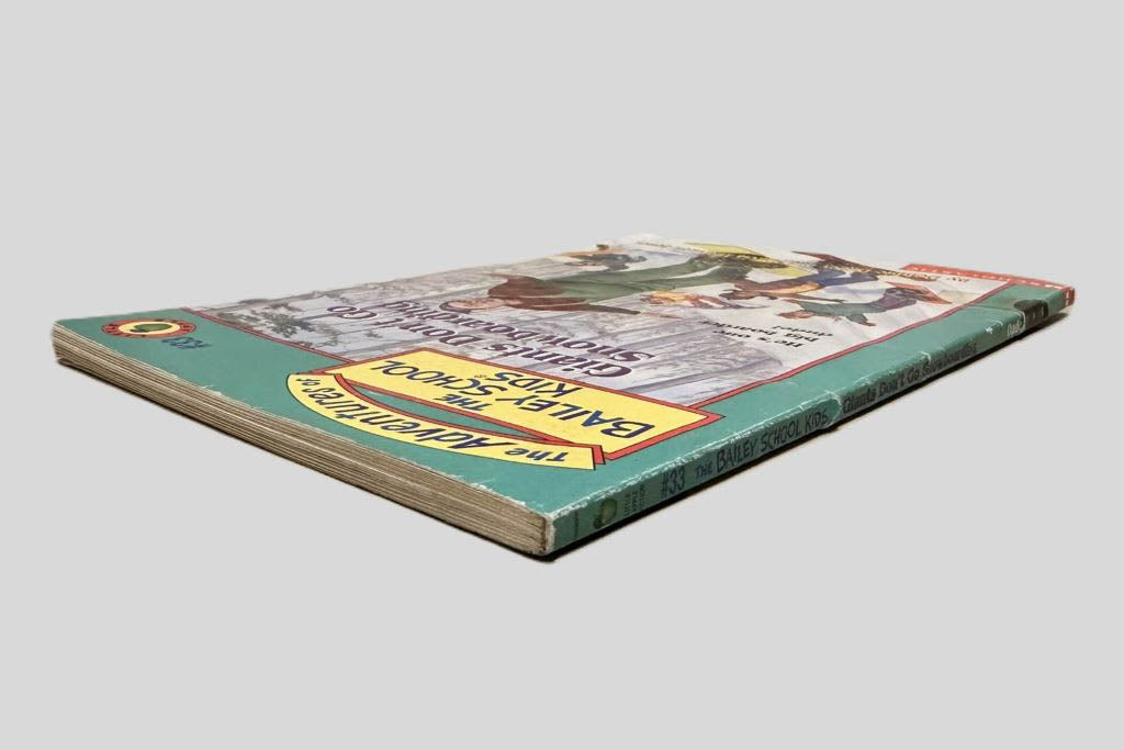 Close-up spine view of Giants Don't Go Snowboarding by Debbie Dadey and Marcia Thornton Jones centered on a neutral light gray background. Spine shows creasing. Pages lay flat.