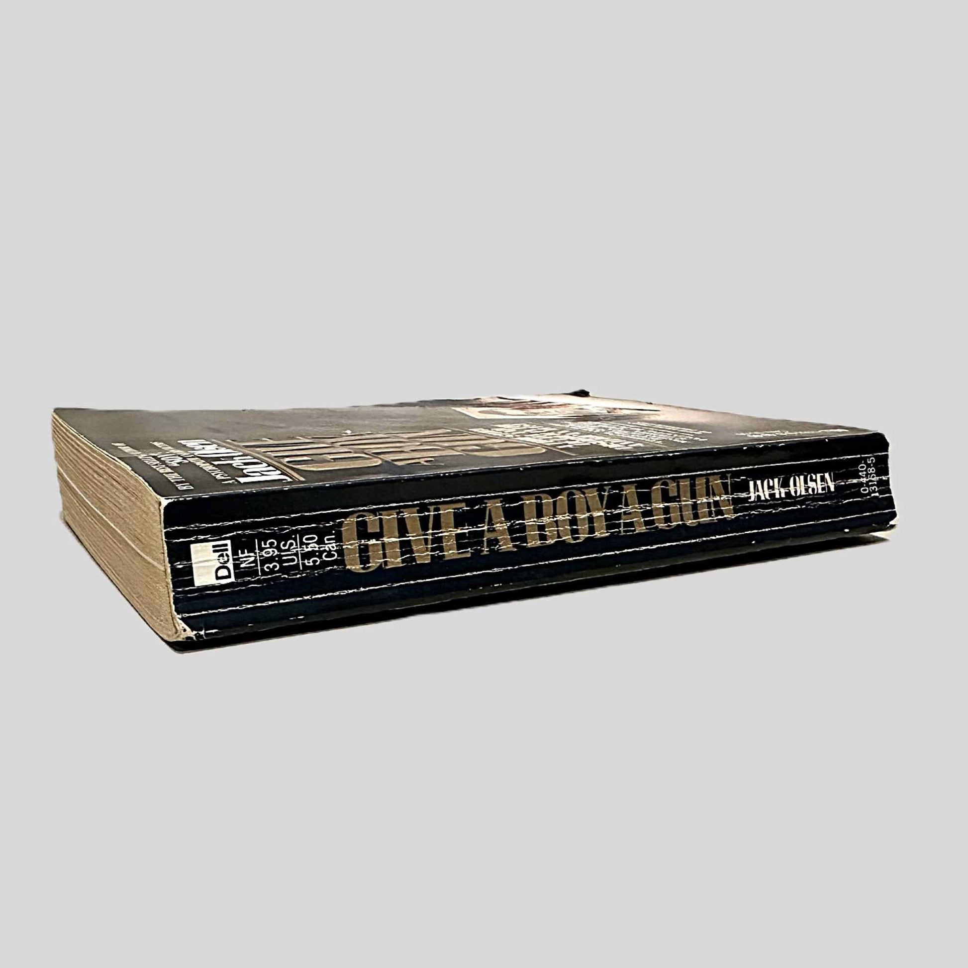 Close-up spine view of Give A Boy A Gun by Jack Olsen centered on a neutral light gray background. Spine shows creasing and bumping.