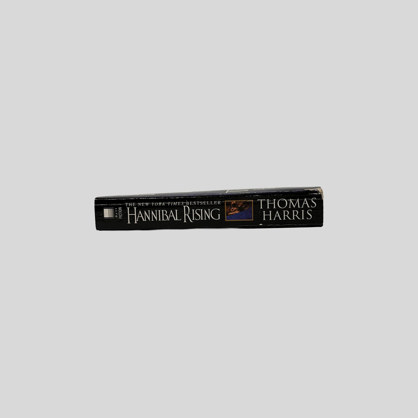 The black spine of the book Hannibal Rising by Thomas Harris, displaying the title in gold serif font alongside a small inset photo of the eye from the front cover.