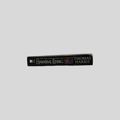 The black spine of the book Hannibal Rising by Thomas Harris, displaying the title in gold serif font alongside a small inset photo of the eye from the front cover.