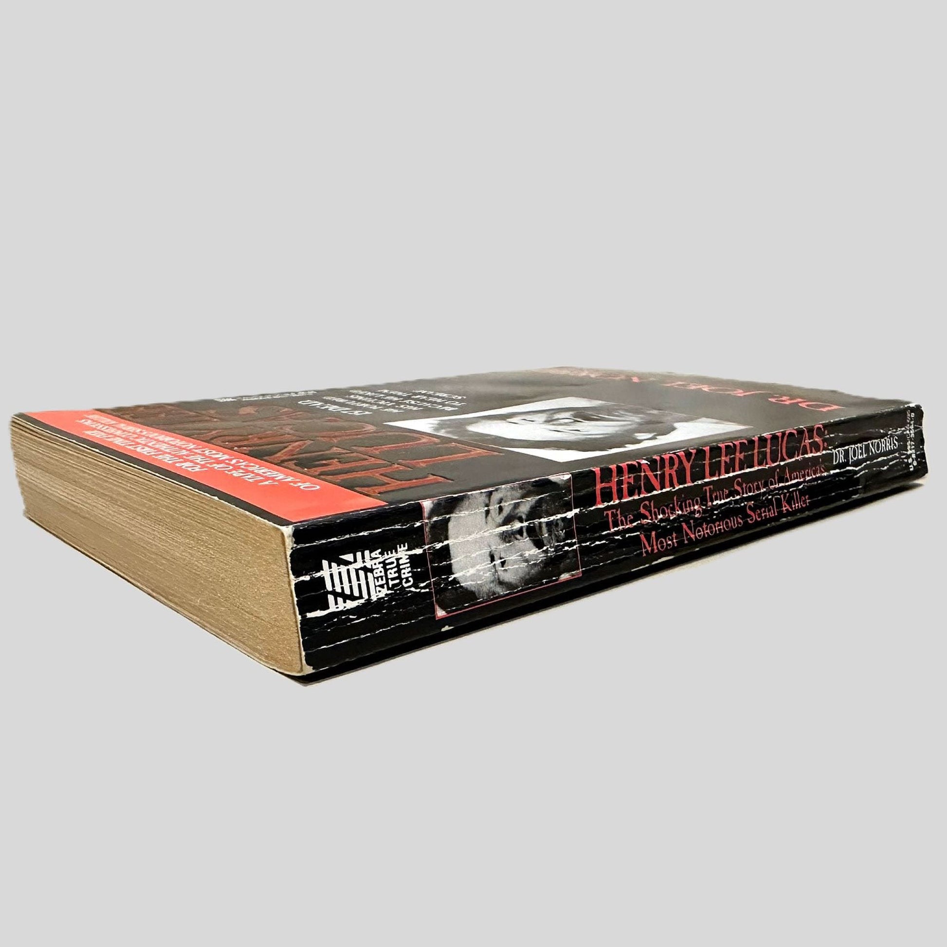 Close-up spine view of Henry Lee Lucas by Dr. Joel Norris centered on a neutral light gray background. Spine shows creasing and rubbing.