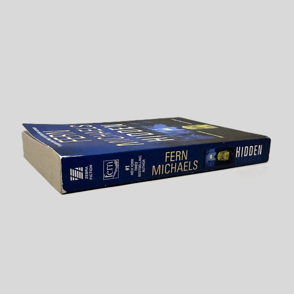 Close-up spine view of Hidden by Fern Michaels centered on a neutral light gray background. Spine shows some chipping at the top corners. Spine is square.