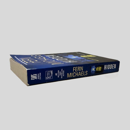 Close-up spine view of Hidden by Fern Michaels centered on a neutral light gray background. Spine shows some chipping at the top corners. Spine is square.