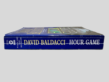 Close-up spine view of Hour Game by David Baldacci centered on a neutral light gray background. Spine shows creasing. Pages lay flat.