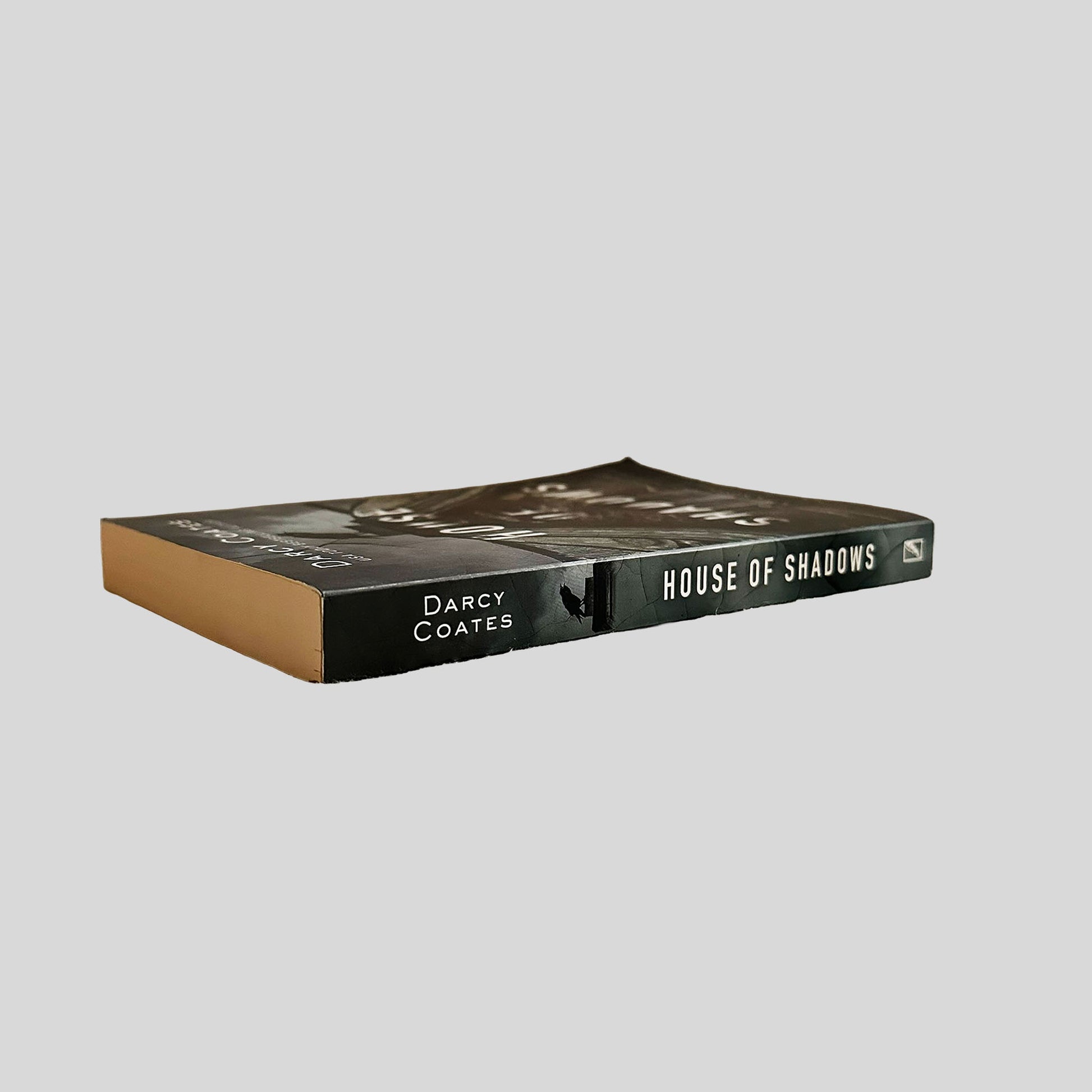 Close-up spine view of House of Shadows by Darcy Coates centered on a neutral light gray background.
