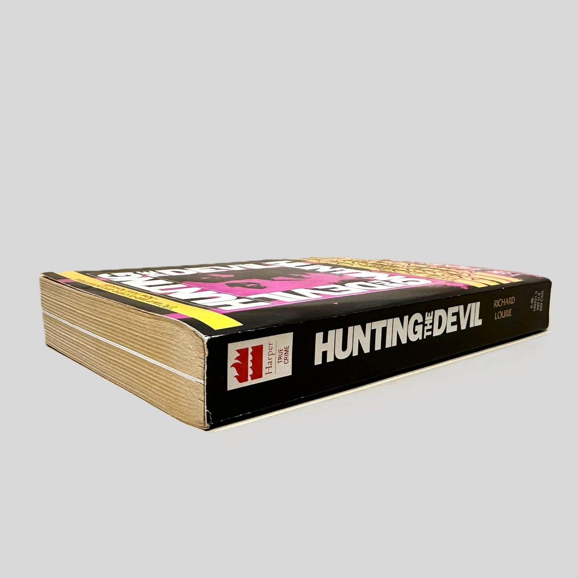 Close-up spine view of Hunting the Devil by Richard Lourie centered on a neutral light gray background. Spine is square and shows minimal creasing.