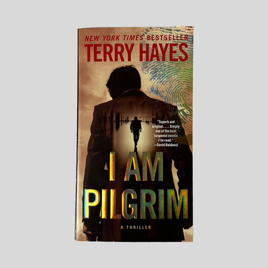 The front cover of the paperback I Am Pilgrim by Terry Hayes, featuring a dark silhouette of a man walking into a bright tunnel with iridescent, holographic title text.