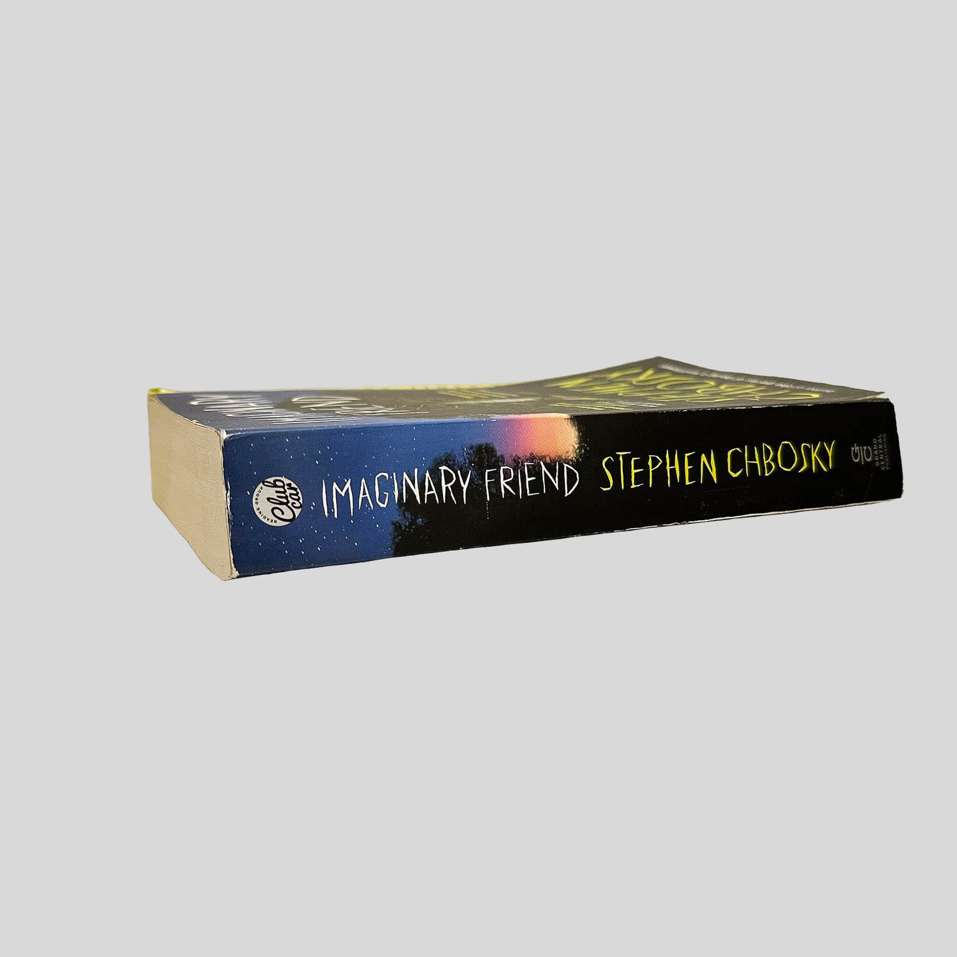 Close-up spine view of Imaginary Friend by Stephen Chbosky centered on a neutral light gray background. Spine shows minimal creasing. Pages lay flat.