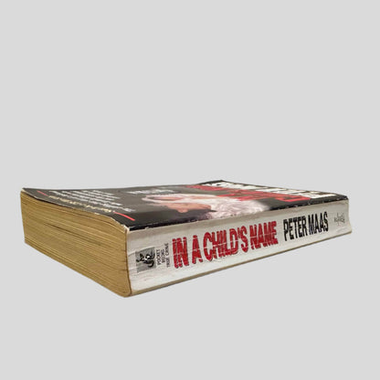 Close-up spine view of In A Child's Name by Peter Maas centered on a neutral light gray background. Spine shows creasing and rubbing.