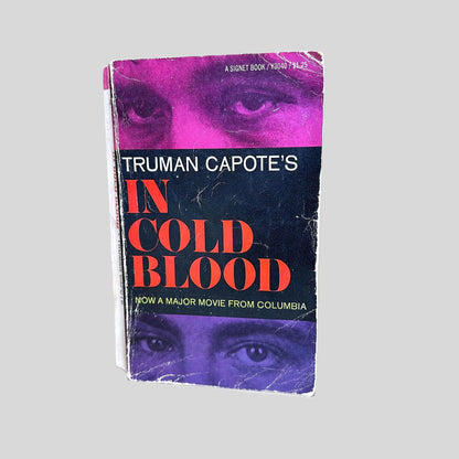 Front cover view of In Cold Blood by Truman Capote with magenta and purple imagery, centered on a neutral light gray background. The cover shows wear from age with rubbing and bumping to the corners.