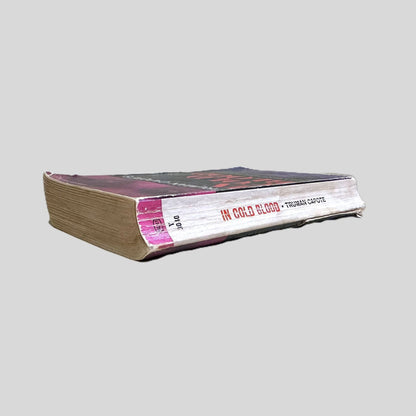 Close-up spine view of In Cold Blood by Truman Capote centered on a neutral light gray background. The spine shows creasing and a cocked spine.