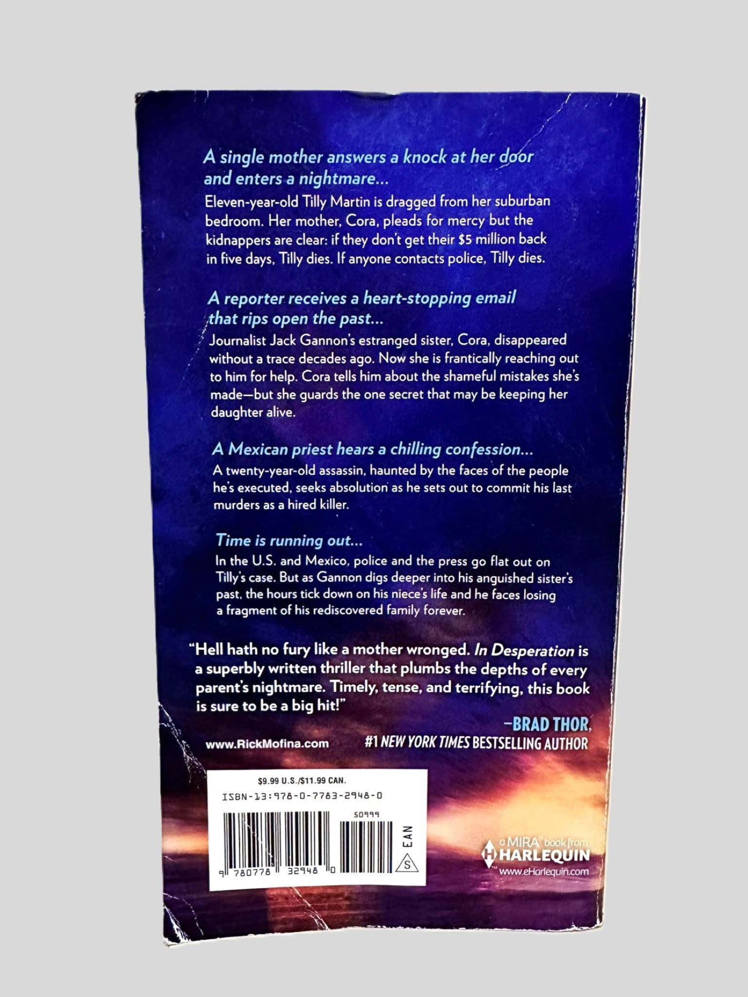 Back cover view of In Desperation by Rick Mofina centered on a neutral light gray background. Some creasing is present on the bottom corner of the cover.