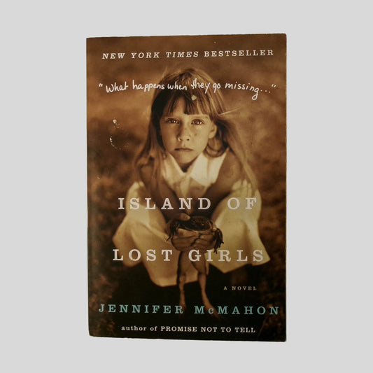 Front cover view of Island of Lost Girls by Jennifer McMahon centered on a neutral light gray background. Minor chipping to the top and bottom of the front cover.