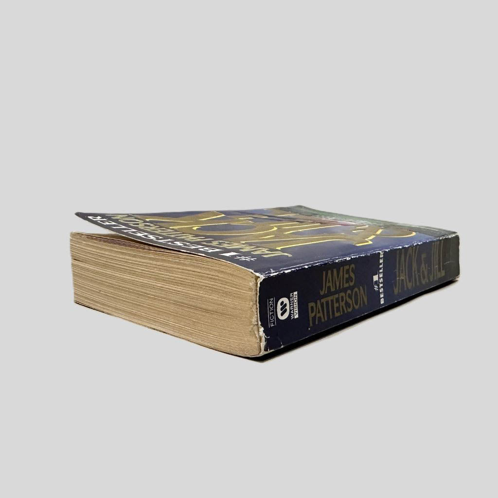 Close-up spine view of Jack & Jill by James Patterson centered on a neutral light gray background. Spine shows minimal creasing and chipping to the top of the spine edge. Pages lay flat.