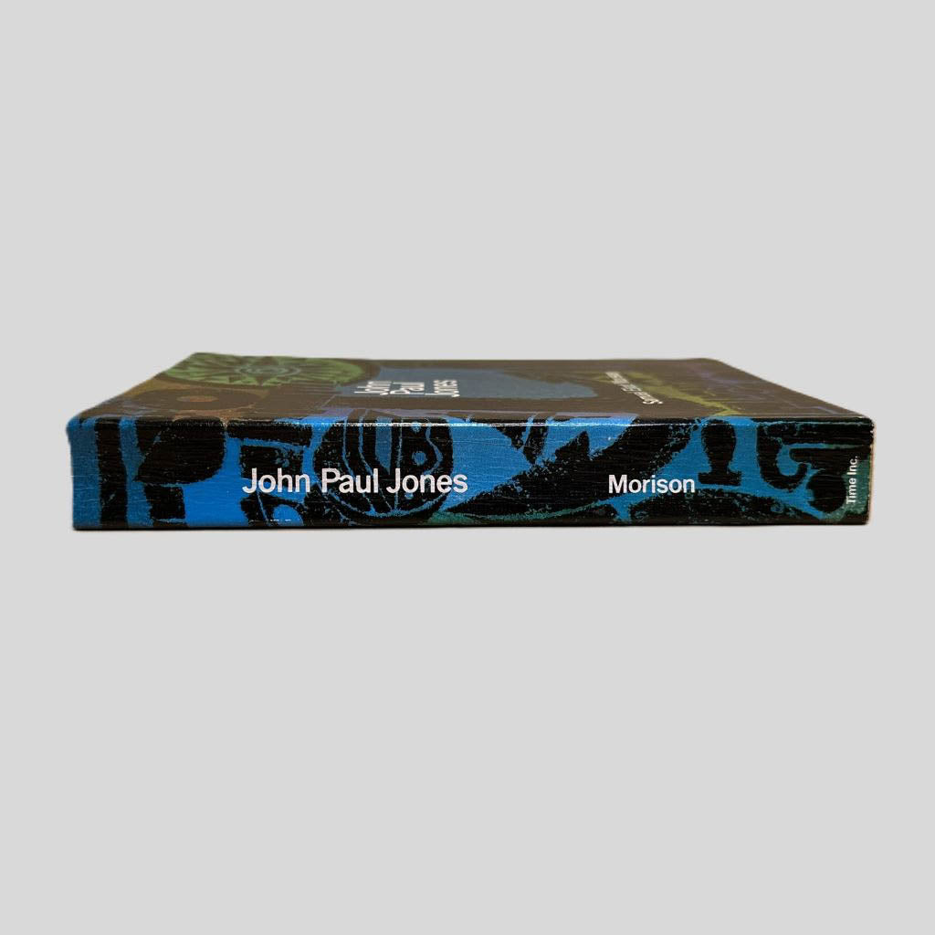 Close-up spine view of John Paul Jones A Sailor’s Biography by Samuel Eliot Morison centered on a neutral light gray background. Spine is square and shows minimal creasing. Pages lay flat.