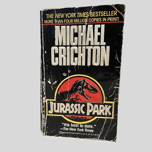 Front cover view of Jurassic Park by Michael Crichton centered on a neutral light gray background. Cover shows extensive creasing, rubbing, and chipping.