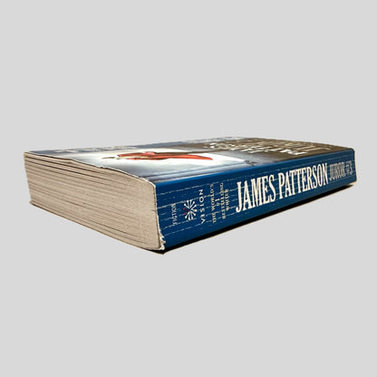 Close-up spine view of Juror #3 by James Patterson centered on a neutral light gray background. Spine shows creasing and chipping at the top corner. Pages lay flat.