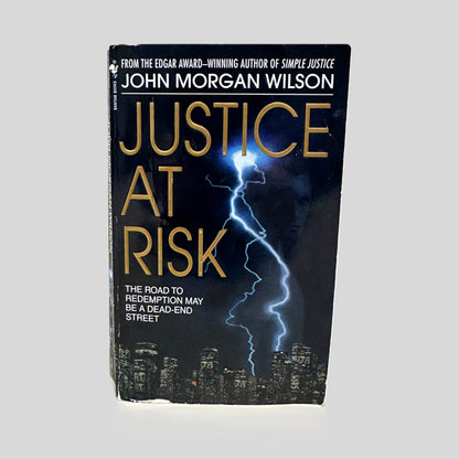 Front cover view of Justice at Risk by John Morgan Wilson centered on a neutral light gray background. Chipping is present along the bottom edge.