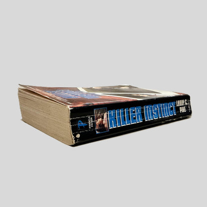 Close-up spine view of Killer Instinct by Larry C Pike centered on a neutral light gray background. Spine shows creasing. Pages lay flat.