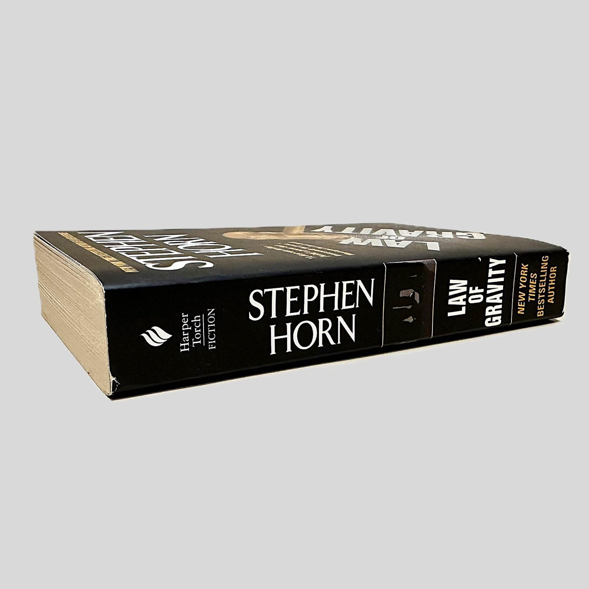 Close-up spine view of Law of Gravity by Stephen Horn centered on a neutral light gray background. Spine is square and shows no creasing. Pages lay flat.