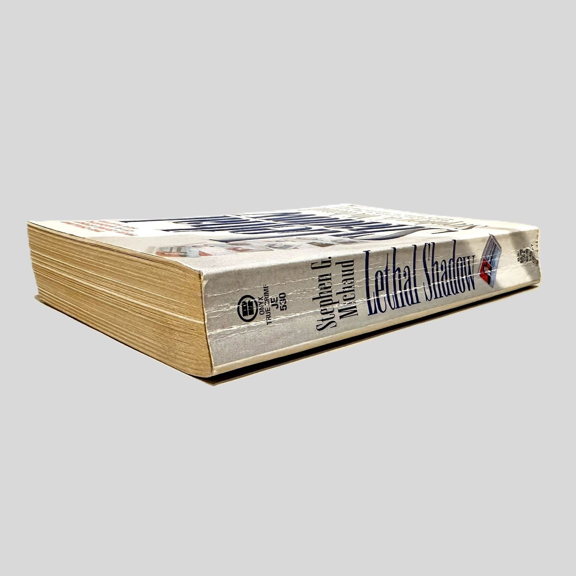 Close-up spine view of Lethal Shadow by Stephen G. Michaud centered on a neutral light gray background. Spine shows minimal creasing.
