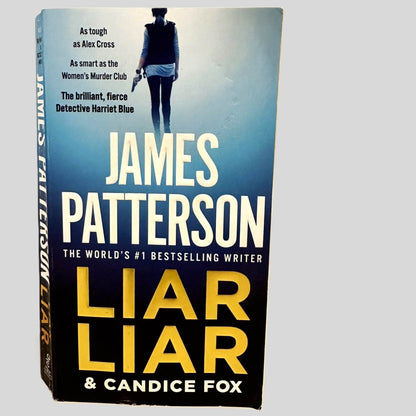 Front cover view of Liar Liar by James Patterson & Candice Fox centered on a neutral light gray background. Chipping present along the bottom edge of the front cover.