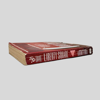 Close-up spine view of Liberty Square by Katherine V Forrest centered on a neutral light gray background. Spine shows creasing. Pages lay flat.