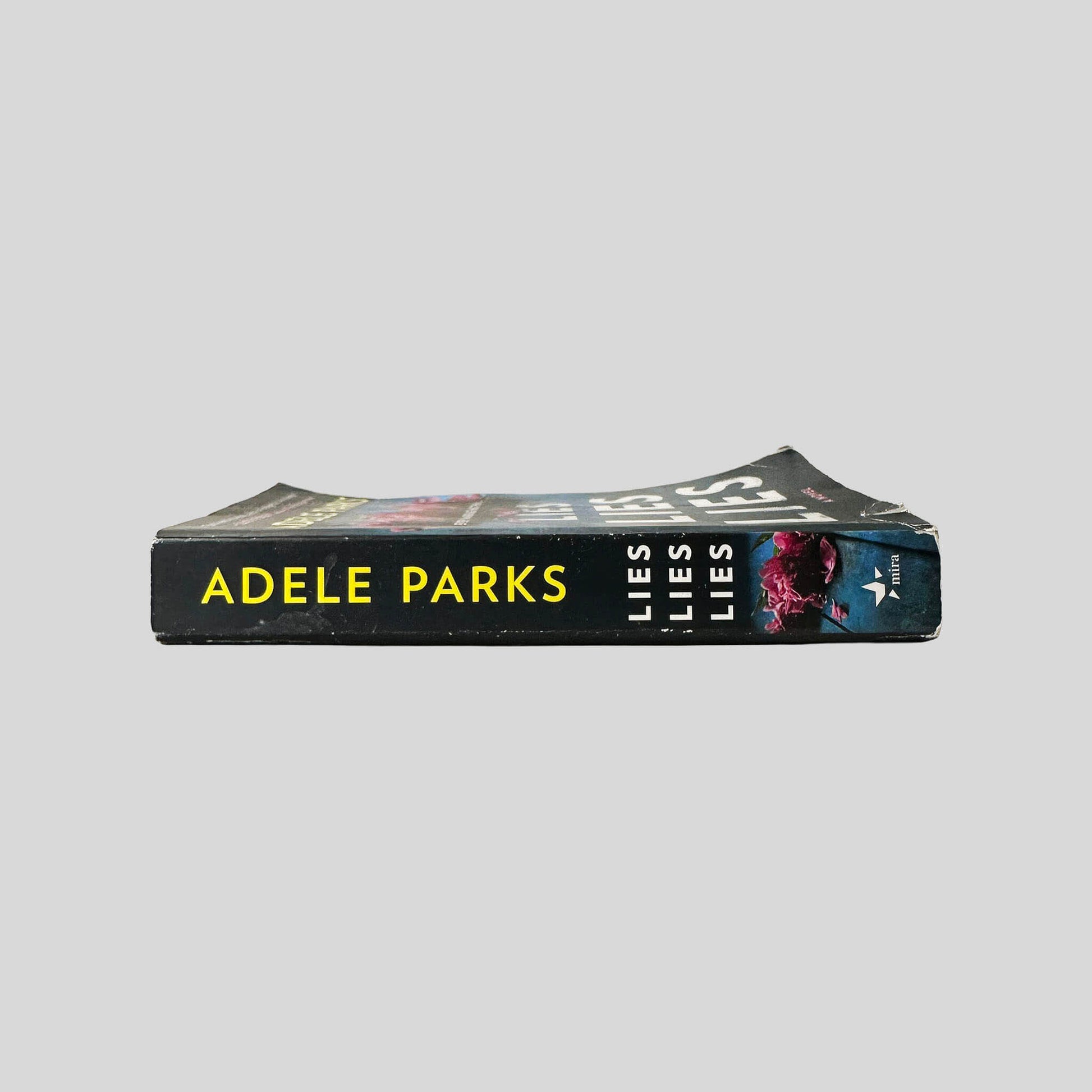Close-up spine view of Lies Lies Lies by Adele Parks centered on a neutral light gray background. Spine shows minimal creasing. Pages lay flat.