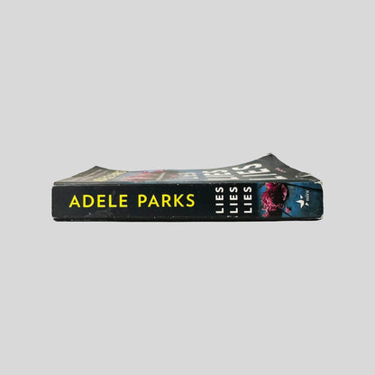 Close-up spine view of Lies Lies Lies by Adele Parks centered on a neutral light gray background. Spine shows minimal creasing. Pages lay flat.