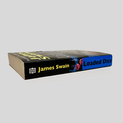 Close-up spine view of Loaded Dice by James Swain centered on a neutral light gray background. Spine shows minimal creasing. Pages lay flat.