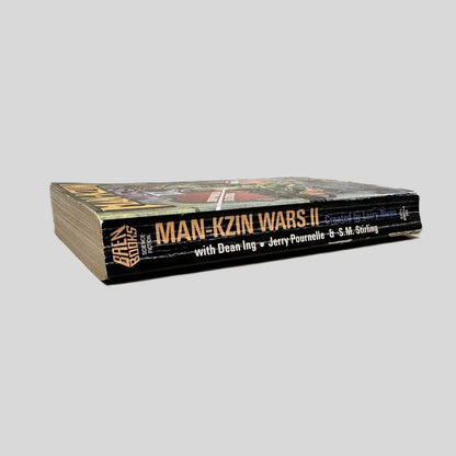 Close-up spine view of Man-Kzin Wars II by Larry Niven centered on a neutral light gray background. Spine shows creasing and chipping at the bottom end. Pages lay flat.
