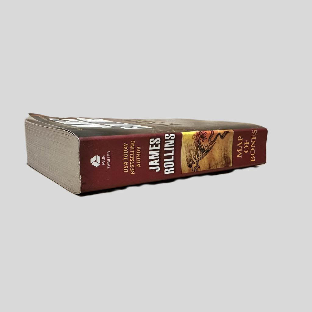 Close-up spine view of Map of Bones by James Rollins centered on a neutral light gray background. Spine is square and shows no visible creasing. Pages lay flat.