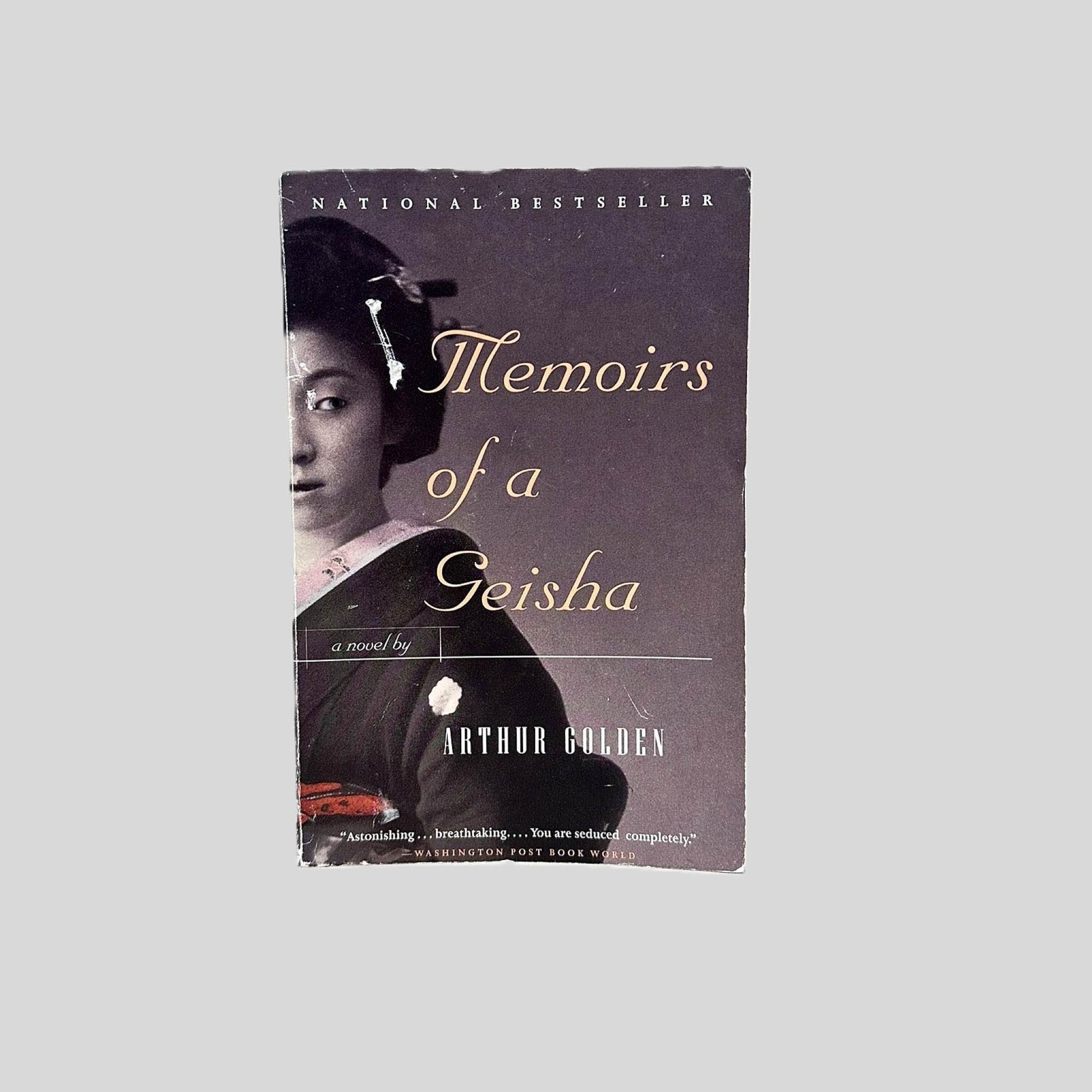 Front cover view of Memoirs of a Geisha by Arthur Golden centered on a neutral light gray background. Minor chipping and creasing around the edges from normal wear and age.