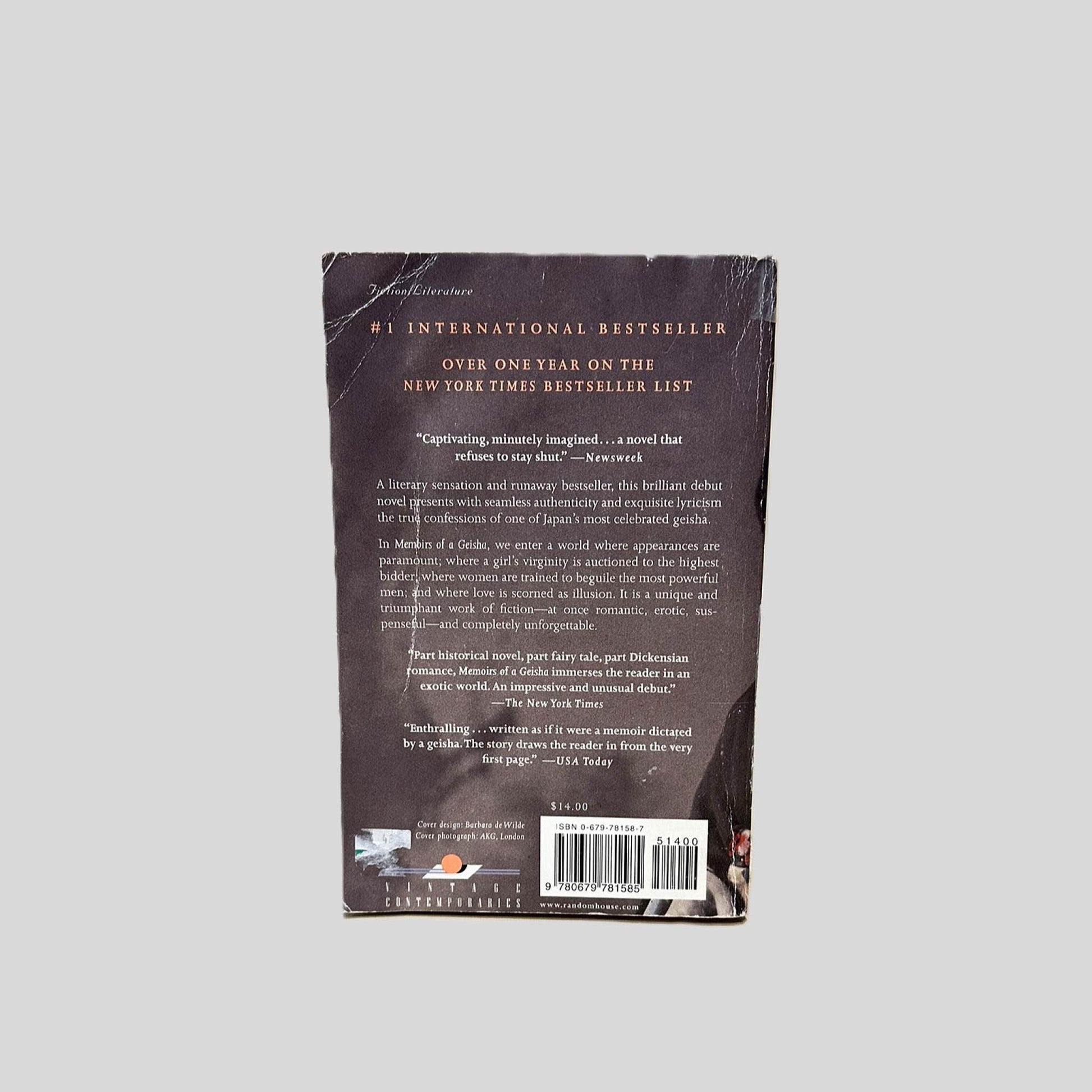 Back cover view of Memoirs of a Geisha by Arthur Golden centered on a neutral light gray background. Deep creasing across top left corner. Creasing is also present near the spine.