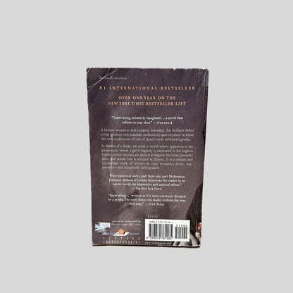 Back cover view of Memoirs of a Geisha by Arthur Golden centered on a neutral light gray background. Deep creasing across top left corner. Creasing is also present near the spine.