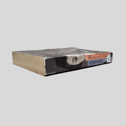Close-up spine view of Memoirs of a Geisha by Arthur Golden centered on a neutral light gray background. Spine is square and shows minimal creasing. Some of the back pages have a wave visible at the page edge.