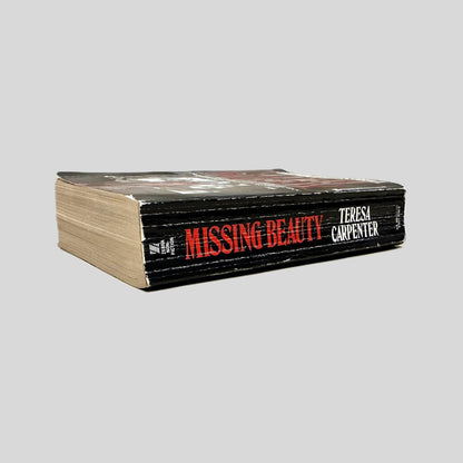 Close-up spine view of Missing Beauty by Teresa Carpenter centered on a neutral light gray background. Spine shows creasing and rubbing.
