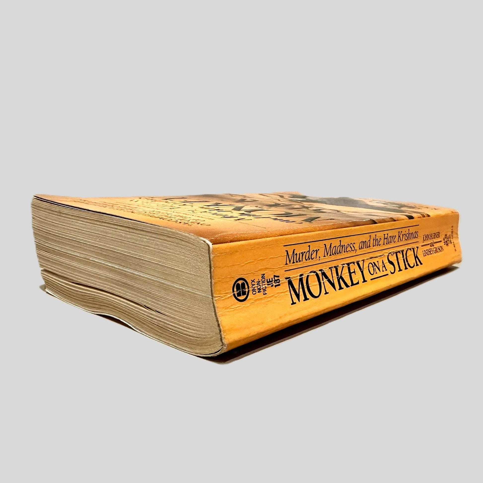 Close-up spine view of Monkey on a Stick by John Hubner & Lindsey Gruson centered on a neutral light gray background. Spine shows creasing and cocking.