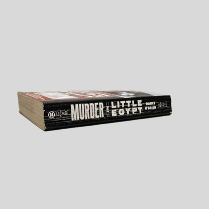 Close-up spine view of Murder in Little Egypt by Darcy O'Brien centered on a neutral light gray background. Spine shows creasing and rubbing.
