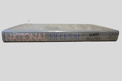 Close-up spine view of National Defense by James Fallows centered on a neutral light gray background. Dust jacket is present and shows no damage. Spine shows no creasing. Pages lay flat.