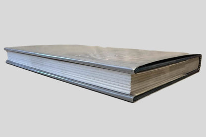 Close-up page edge view of National Defense by James Fallows centered on a neutral light gray background. Dust jacket is present and shows no damage. Spine shows no creasing. Pages lay flat.