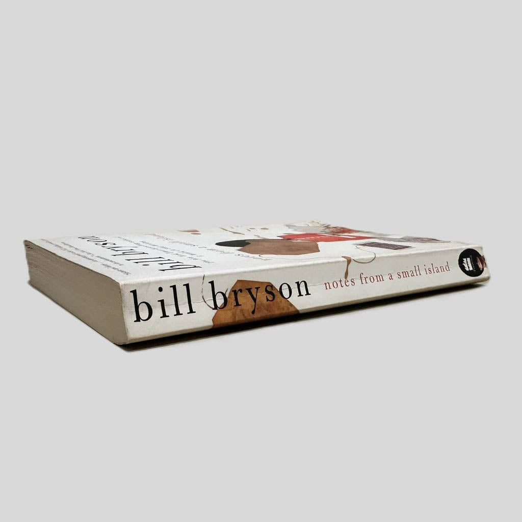 Close-up spine view of Notes from a Small Island by Bill Bryson centered on a neutral light gray background. Spine shows minimal creasing and cocking. Pages lay flat.